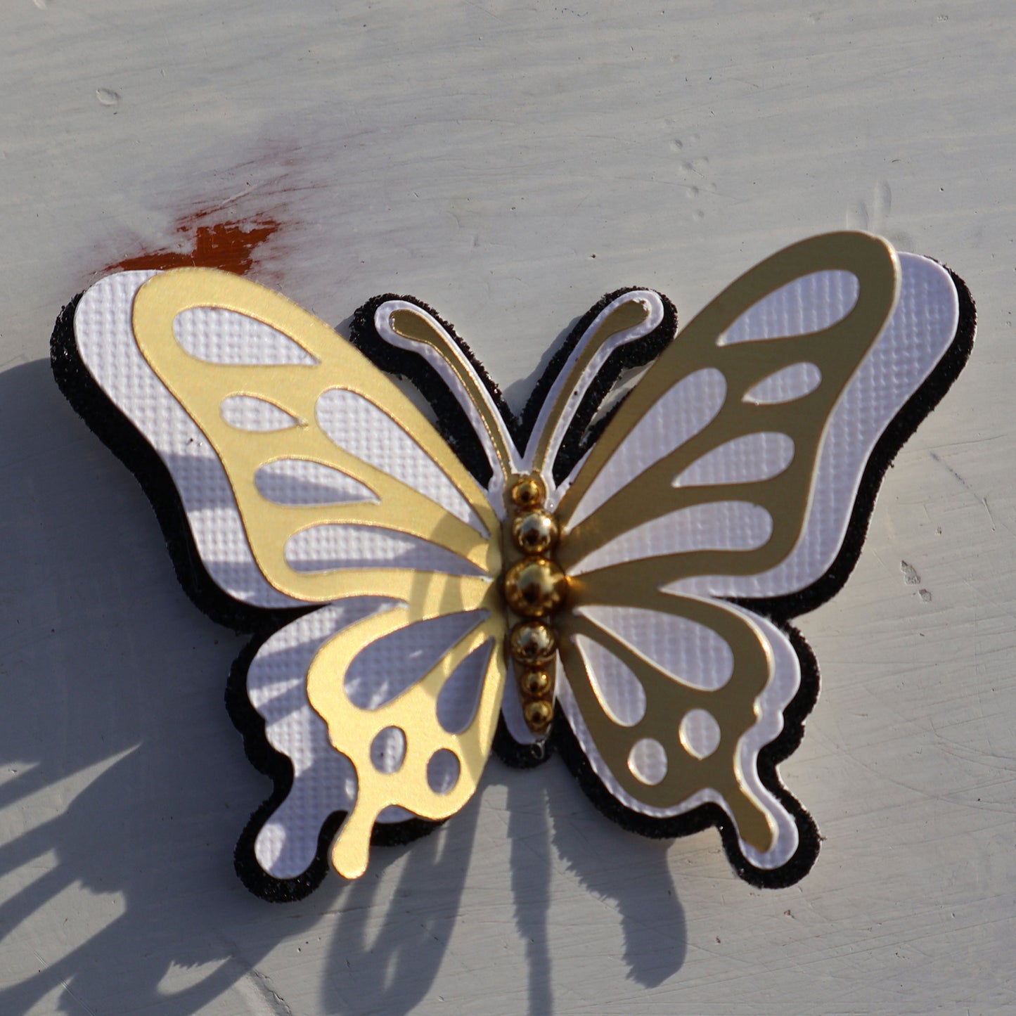 Close-up of a 3D gold and white butterfly spirit cutout showing the layered "flutter" effect and gold bead detail.