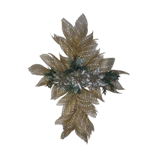 A handcrafted cross-shaped wall wreath made of natural burlap-colored deco mesh with gold metallic stripes and white "snow" accents. The center features three large, shimmering silver-glittered poinsettias surrounded by dark green evergreen sprigs and frosted lamb's ear leaves, set against a clean white background.