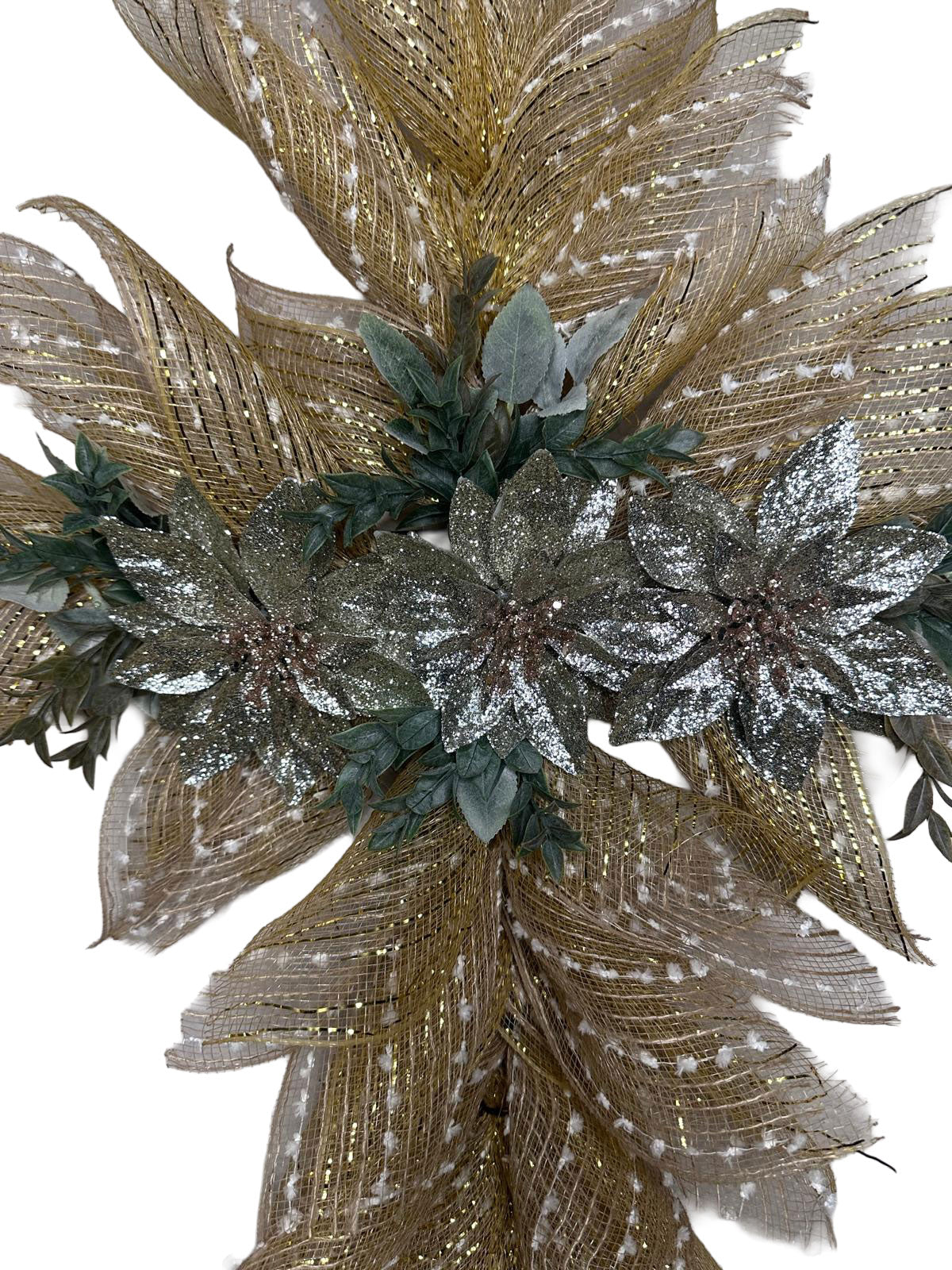 A detailed close-up of a burlap cross wreath highlighting the texture of the gold-striped mesh and white snowy flecks. The focus is on three prominent silver-glittered poinsettias with realistic green foliage and soft, flocked greenery tucked behind the petals for a multidimensional holiday look.