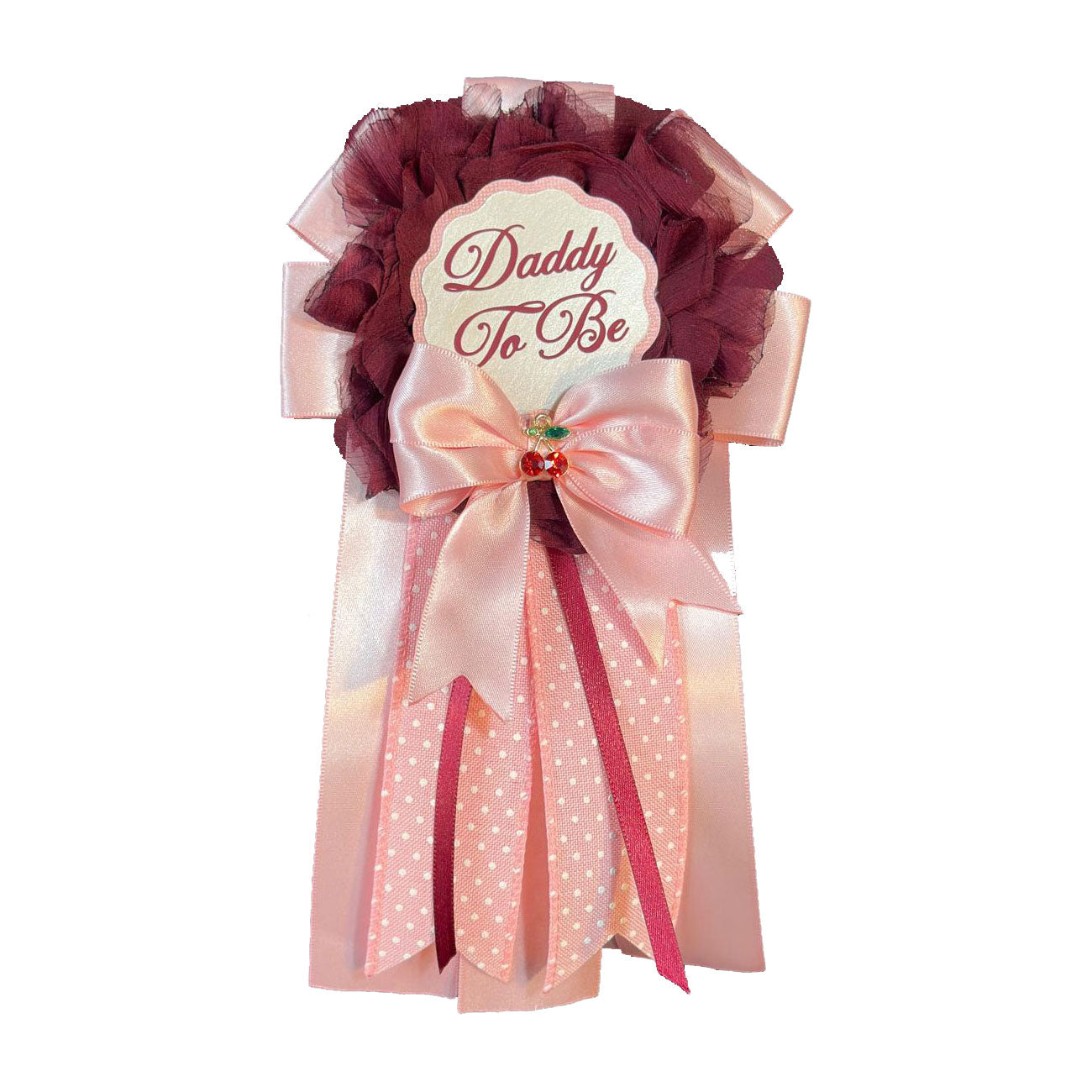Close-up of a handmade Daddy-to-Be award ribbon pin featuring burgundy chiffon, pink satin ribbons, polka-dot accents, and a small cherry embellishment.