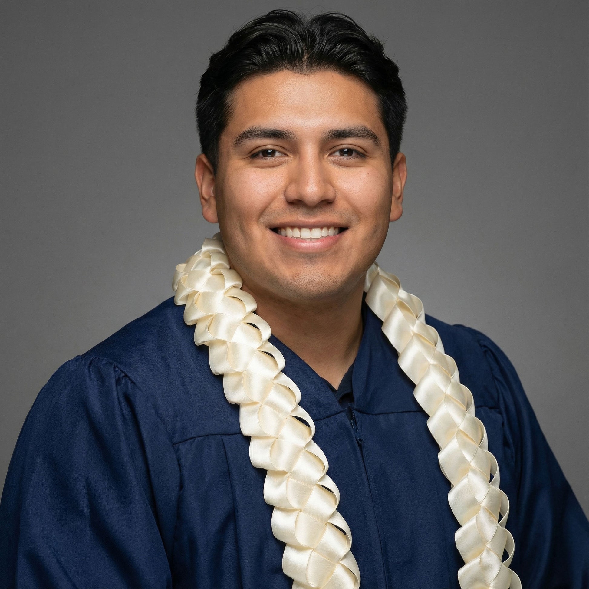 Professional studio portrait of a male graduate in a navy gown wearing a handcrafted solid ivory satin single military braid graduation lei.