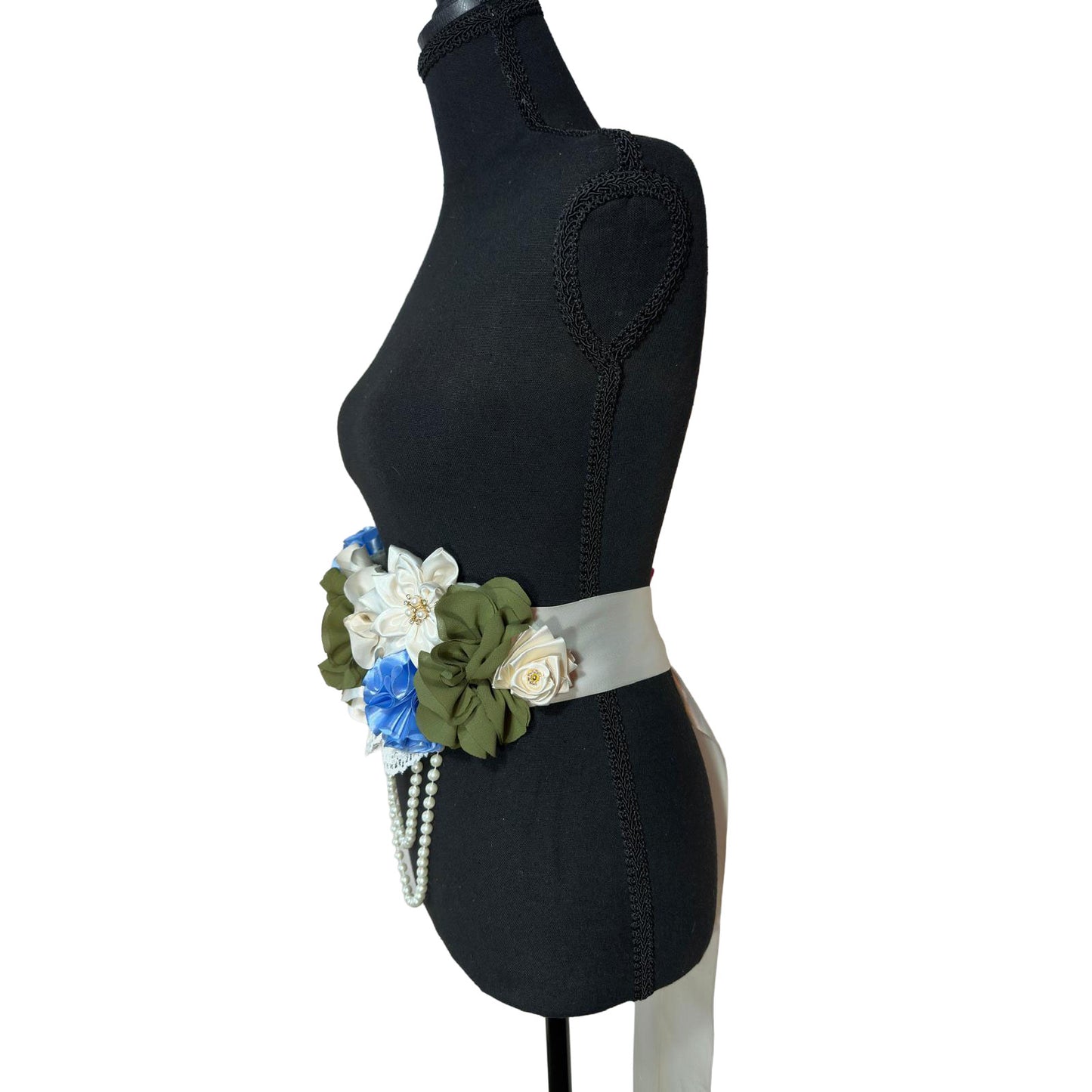 Side profile of a floral maternity sash on a mannequin showing the ivory satin ribbon tie and layered fabric flowers.