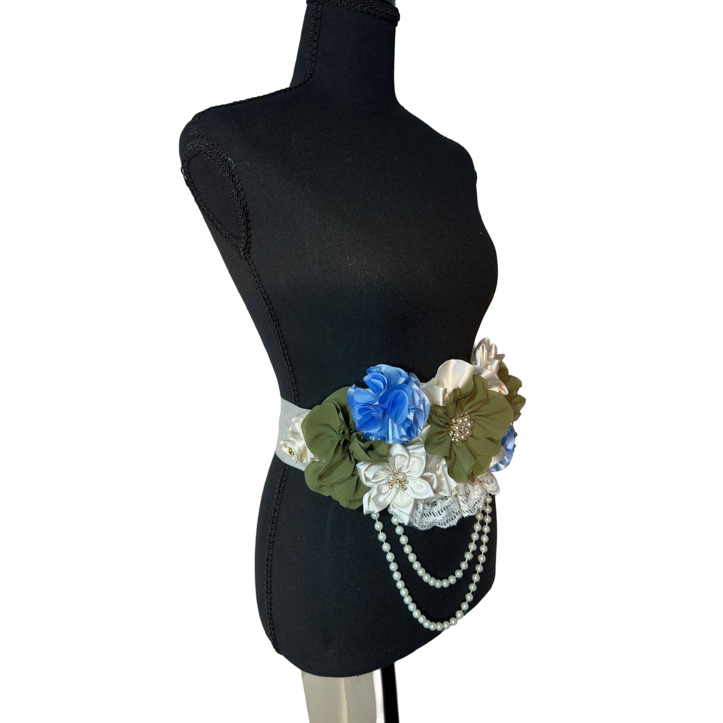 Angled view of a green and light blue maternity flower belt with rhinestone centers and delicate white lace detailing.