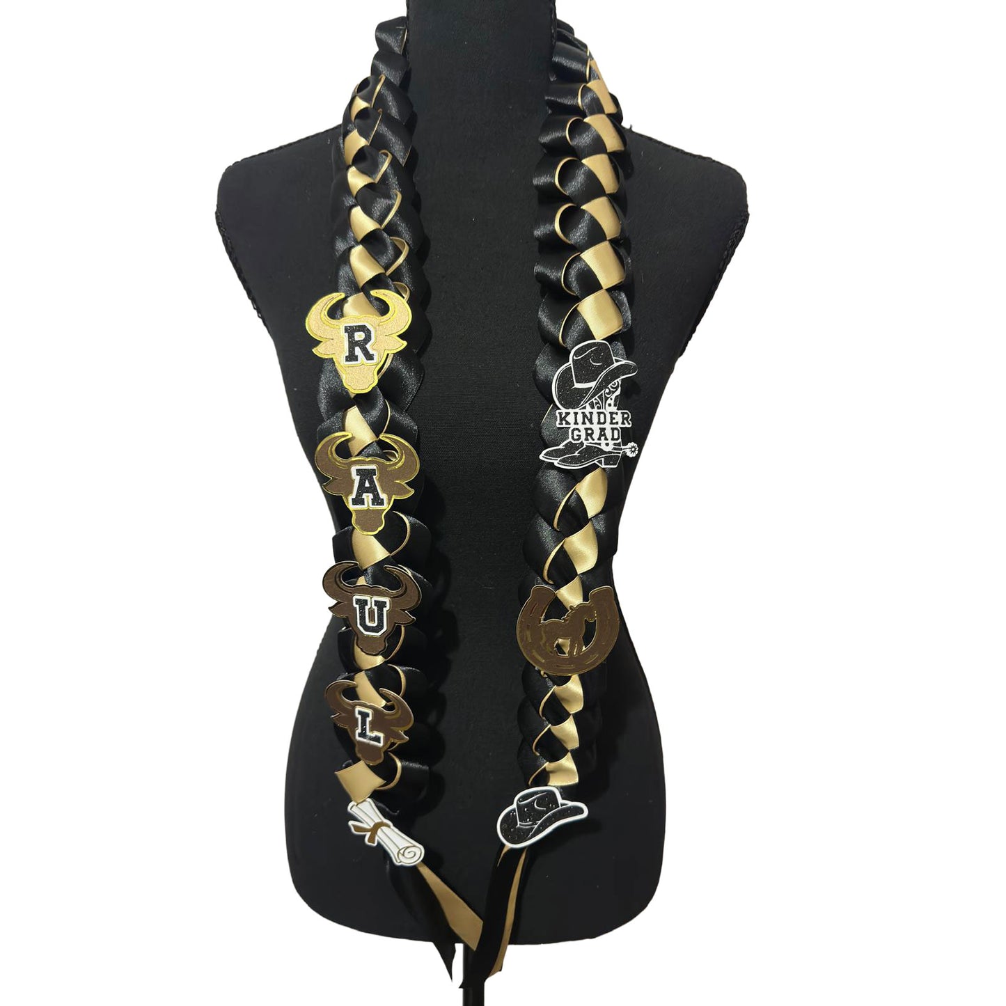 Front view of a custom black and gold braided satin ribbon graduation lei on a black mannequin display, featuring western cowboy theme cutouts and satin streamers.