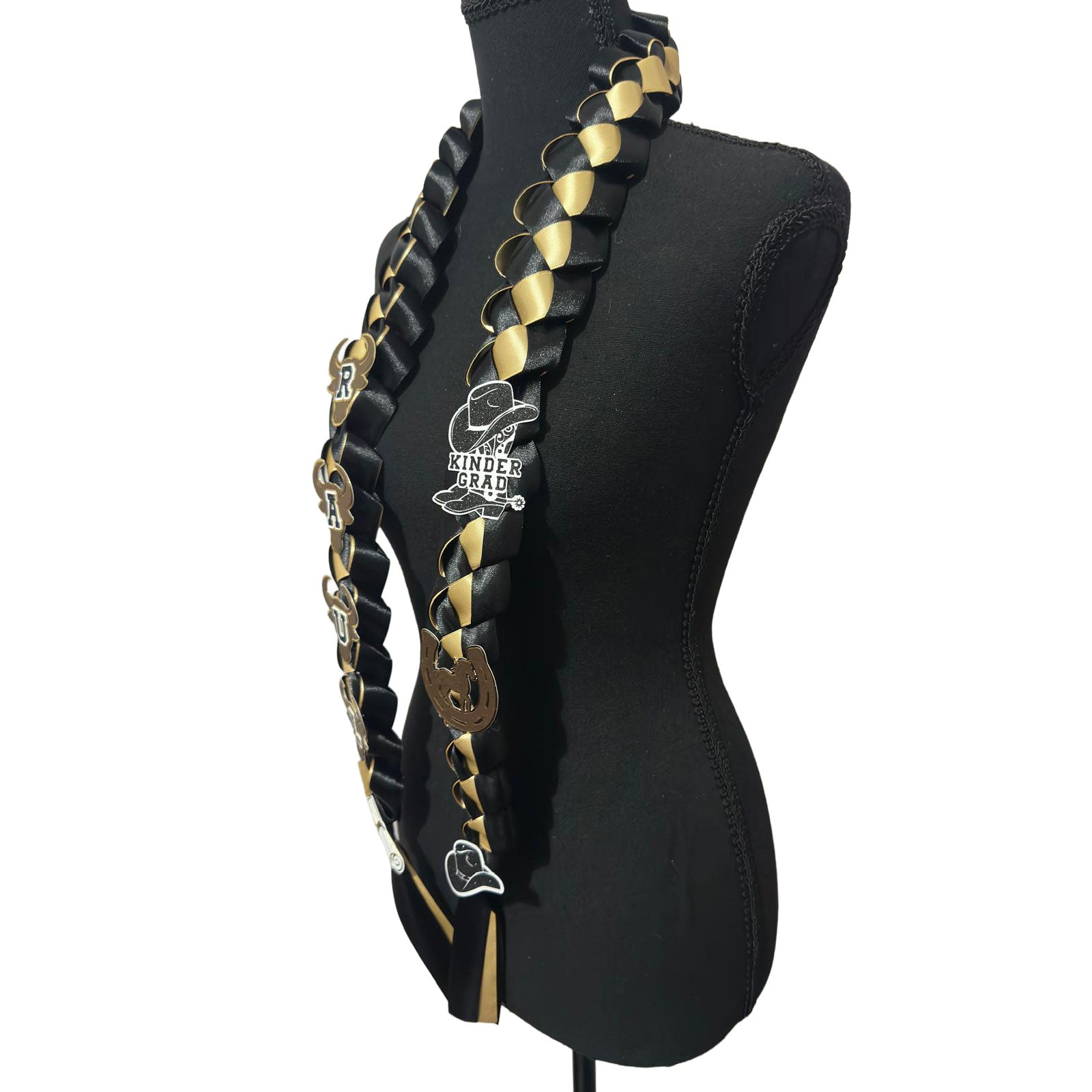 Side view of a custom black and gold braided satin ribbon graduation lei on a black mannequin display, featuring western cowboy theme cutouts and satin streamers.
