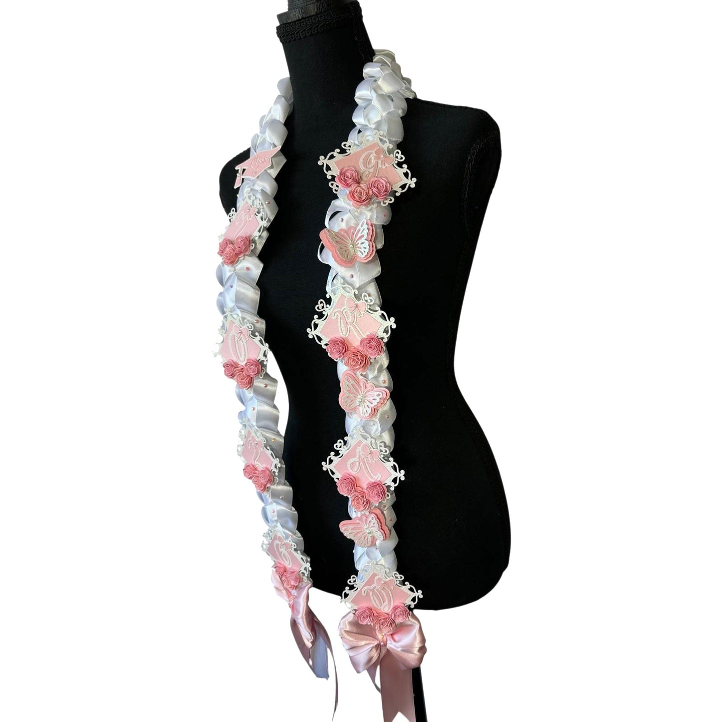 Side profile of a mannequin wearing a handcrafted 2026 graduation lei highlighting the intricate white satin military braid, layered pink and white butterflies, and large shimmering pink satin bows at the base.