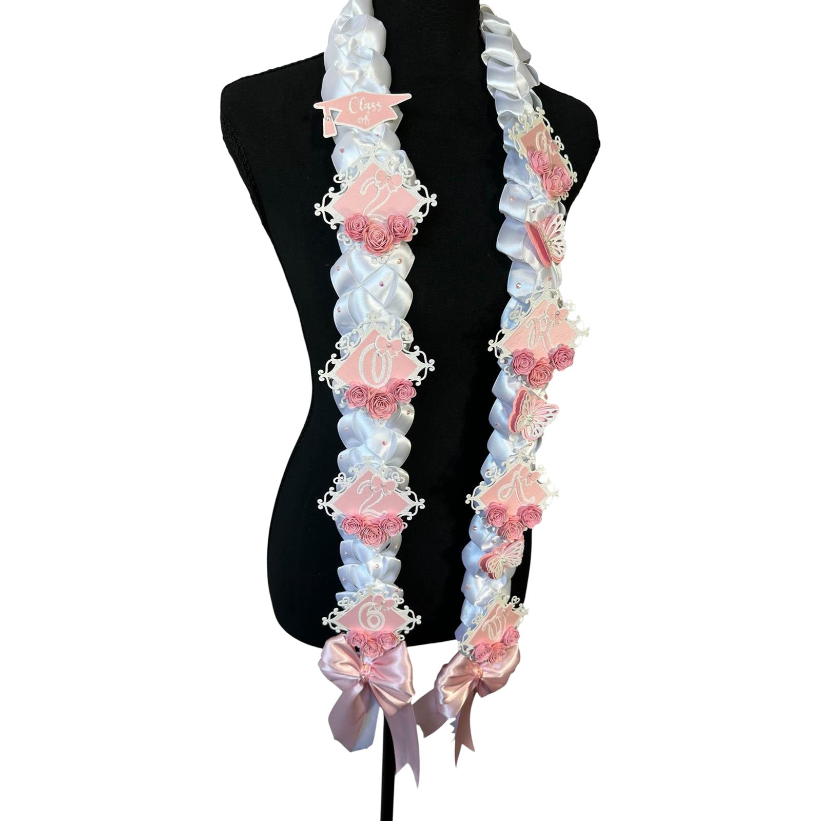 Side profile of a handcrafted 2026 graduation lei highlighting the intricate white satin military braid, layered pink and white butterflies, and large shimmering pink satin bows at the base.