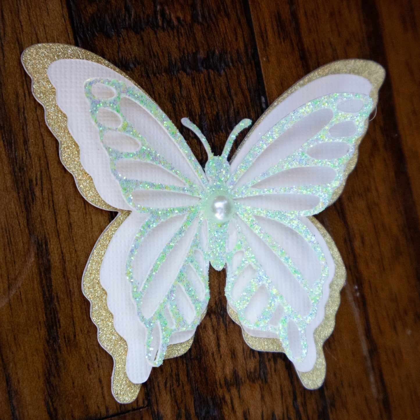 3D mint green and gold butterfly spirit cutout displayed on a dark wood surface to highlight the iridescent glitter.