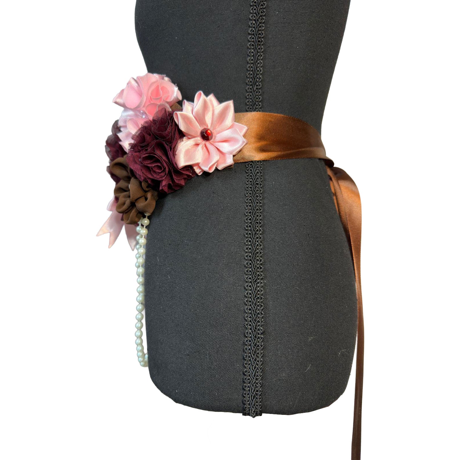 Side profile of the floral maternity sash showing the brown satin ribbon tie and the layered detail of the pink and burgundy fabric flowers.