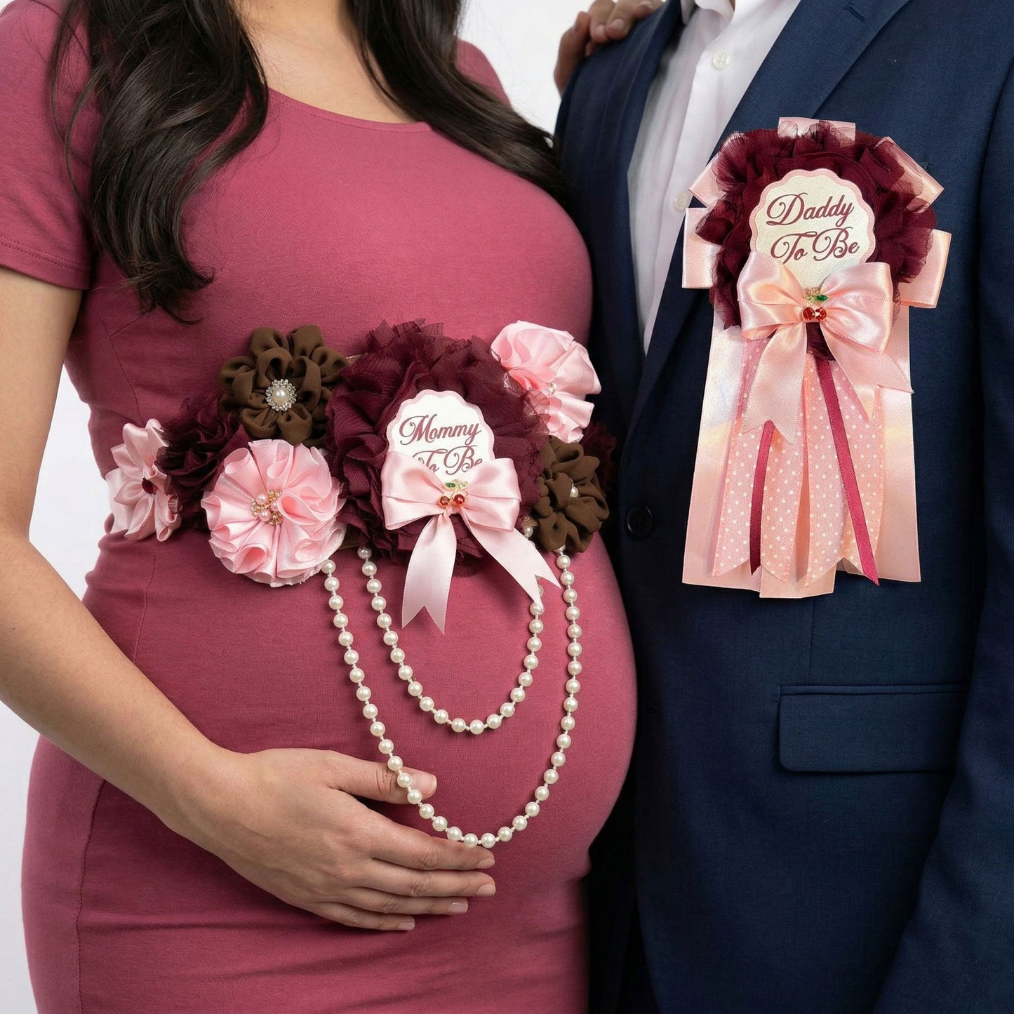 Lifestyle shot of a pregnant woman wearing a burgundy and pink floral maternity sash and a man in a navy suit wearing a matching Daddy-to-Be pin.