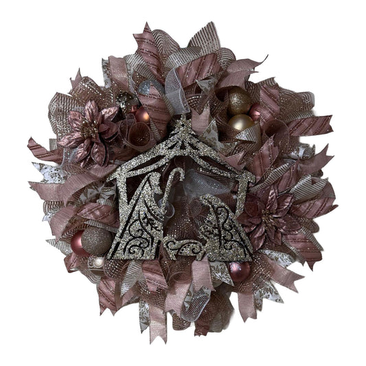 Decorative wreath with ribbons, ornaments, and rose gold nativity in the center on a white background.