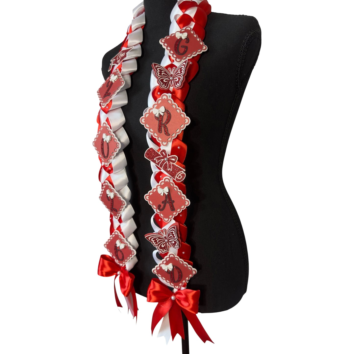 A three-quarter side view of a Red and White Single Military Braid Graduation Lei on a black mannequin torso, showcasing the left-side ribbon detail featuring the 'G', 'R', 'A', 'D' glitter scalloped charms and a red glitter diploma.